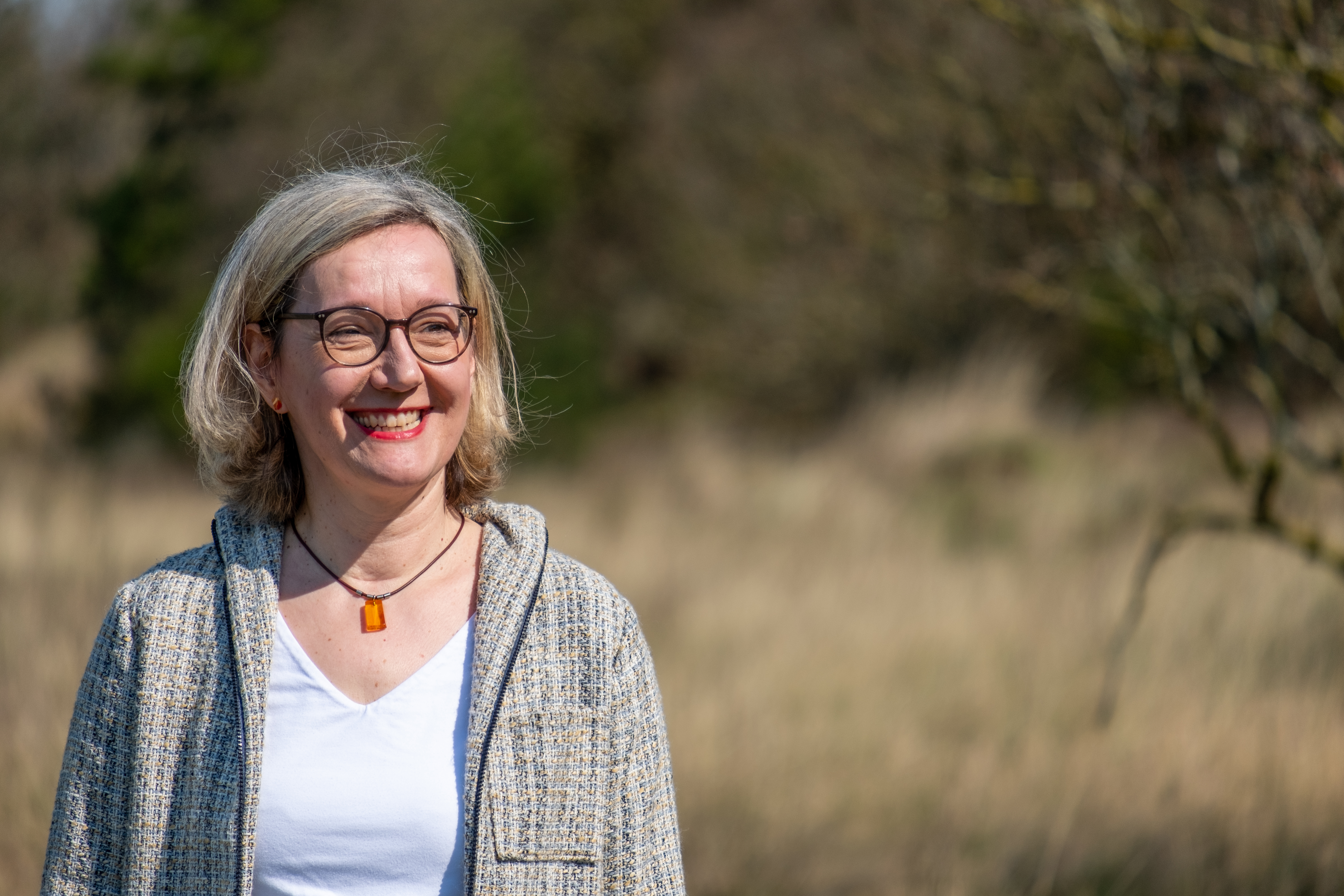 Eine Frau in grauer Jacke in der Natur.